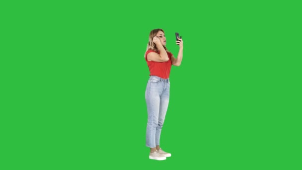 Красивая молодая женщина наносит тушь глядя на свой телефон на зеленом экране, Chroma Key . — стоковое видео