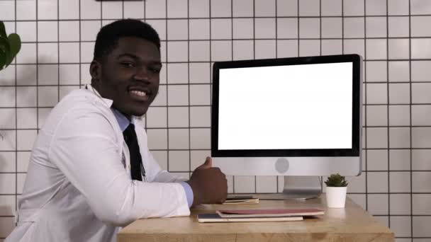 Zwarte dokter praat met camera naast computerscherm. Wit display. — Stockvideo