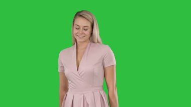 Pembe elbiseli bir yeşil ekranda Chroma Key utangaç kameraya gülümseyen güzel kadın.