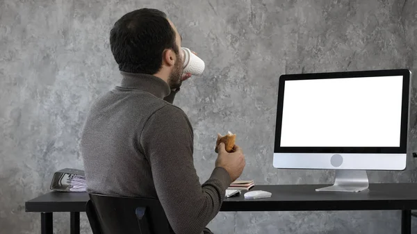 Business man in the office having breakfast, lunch and watching something on the mac, computer. White Display.