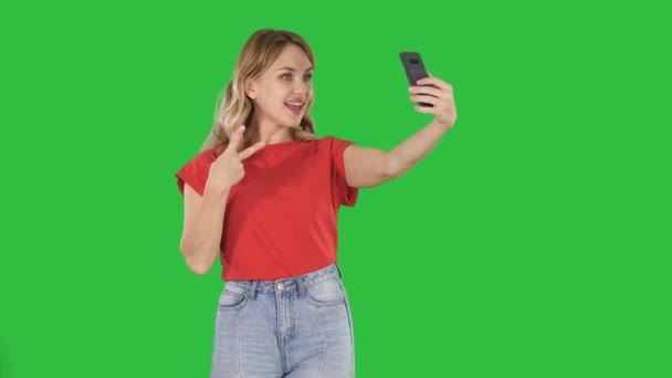 在绿色屏幕上行走时, 身穿红色 t恤的30岁的欢乐女性在绿色屏幕上走着自拍照片. — 图库视频影像