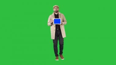 Tam uzunlukta vurdu. Yürüme, konuşma ve dijital tablet ile mavi ekran mockup Chroma Key bir yeşil ekranda gösterilen genç adam. 4 k çözünürlüklü profesyonel vurulmuş. 006. sen-ebilmek kullanma o örneğin,