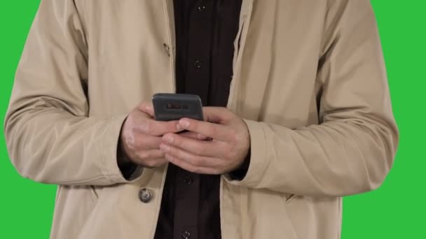 Homem de casaco de trincheira usando celular inteligente em uma tela verde, Chroma Key . — Vídeo de Stock