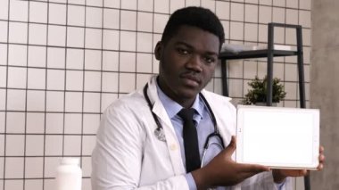 Yakışıklı bir Afrikalı doktor tablet ekranda ürününü sunuyor. Beyaz Görünüm.