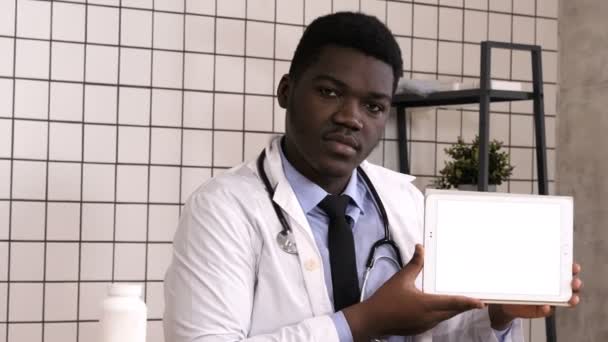 Schöne seriöse afrikanische Arzt präsentiert Produkt auf Tablet-Bildschirm. Weißes Display. — Stockvideo