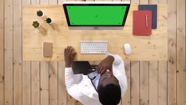 Afrikanischer Arzt, der etwas auf dem Bildschirm des Computers beobachtet. weißes Display. — Stockvideo