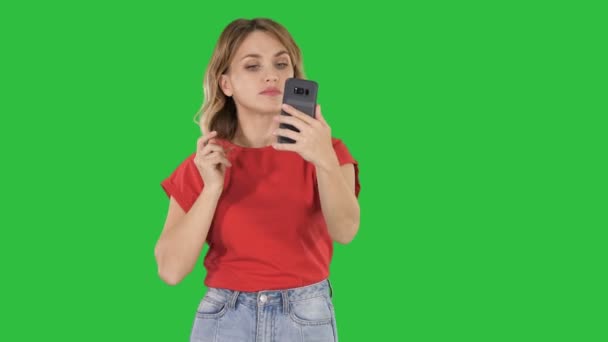 Uma jovem agradável endireita seu cabelo olhando no celular em uma tela verde, Chroma Key . — Vídeo de Stock