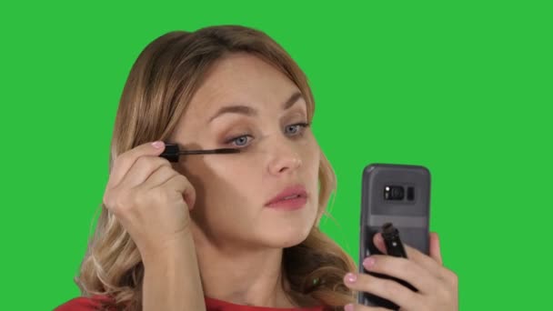クロマキー グリーン画面上の彼女の携帯電話で見ているまつげの黒のマスカラーを適用する女性. — ストック動画