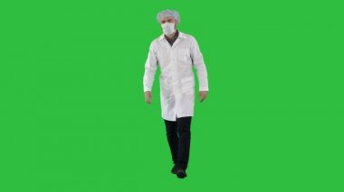 Bir maske ve Chroma Key bir yeşil ekranda tıbbi bir kap içinde yürüyen genç erkek doktor.