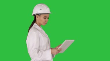 Yeşil ekranda Chroma Key nesnelerini çevreleyen bakarak tablet ile yürüyen genç bir kadın mühendis.