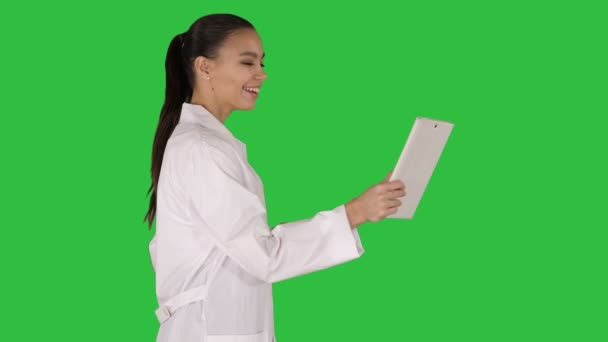 Jonge vrouw arts bedrijf tablet in haar handen en het maken van video-oproep op een groen scherm, Chromakey. — Stockvideo