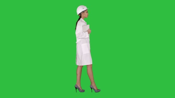 Aantrekkelijke Hispanic vrouw in witte lab jas en witte veiligheid harde hoed wandelen bedrijf laptop of tablet op een groen scherm, Chromakey. — Stockvideo