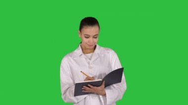 Defter tutan ve yeşil ekranda Chroma Key yürüme yaratıcı fikir ifade genç kadın doktor.