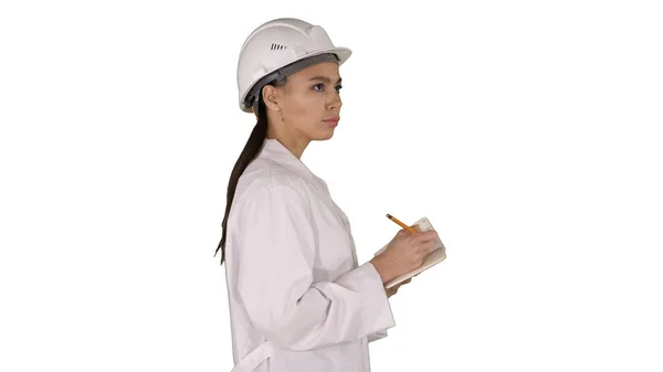 Kobieta inżynier w kasku trzyma pióro i listę kontrolną, kładąc coś na białym tle.. — Zdjęcie stockowe