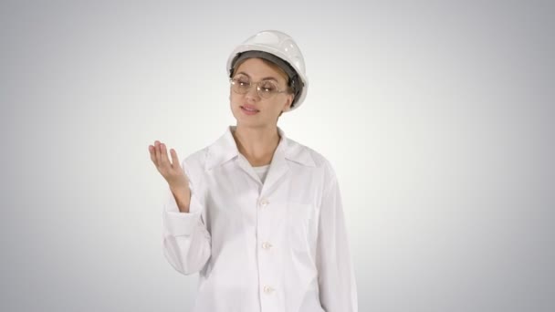Gammal ingenjör kvinna i hård hatt och labbrock prata och presentera något som pekar på sidor på lutning bakgrund. — Stockvideo