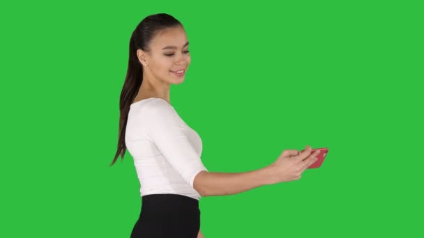 Young brunette taking selfie photo on smartphone smiling joyful and walking on a Green Screen, Chroma Key. — Stock Video