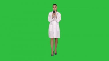 Neşeli sevimli genç kadın doktor Chroma anahtar yeşil ekran yürürken telefonda metin yazma.