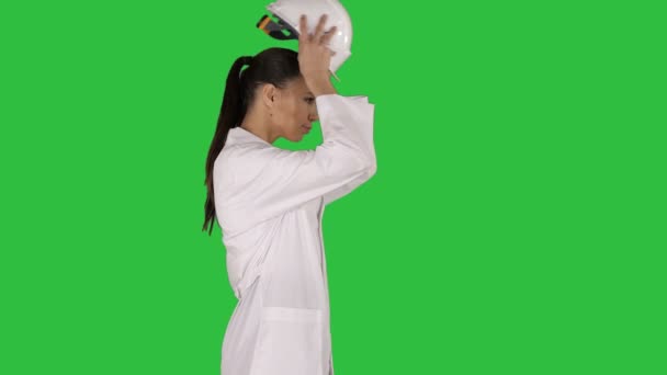 Woman in white robe putting hard hat on while walking on a Green Screen, Chroma Key. — Stock Video