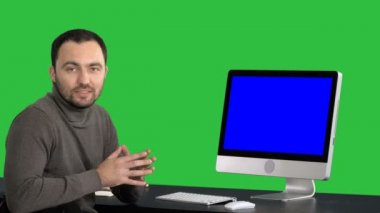 Gülümseyen ve bir şey bilgisayar üstünde a yeşil perde, Chroma Key monitörde gösterilen kameraya konuşurken rahat iş adamı. Mavi ekran Mock-up.