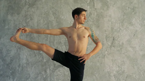 Mestre de ioga masculino alongamento perna no estúdio. De pé, segurando — Fotografia de Stock