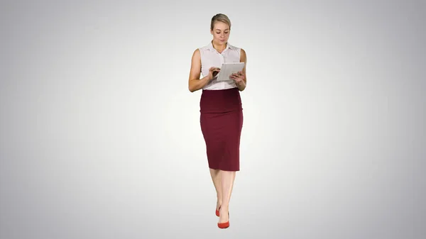 Genç profesyonel iş kadını tablet bilgisayar kullanıyor ve gradyan arka planda kameraya doğru yürüyor.. — Stok fotoğraf