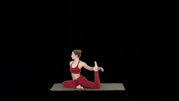 Vacker ung kvinna som bär röd sportkläder gör yoga eller pilates utöva en fyrbent King Pigeon pose, Eka Pada Rajakapotasana, alfakanal — Stockvideo