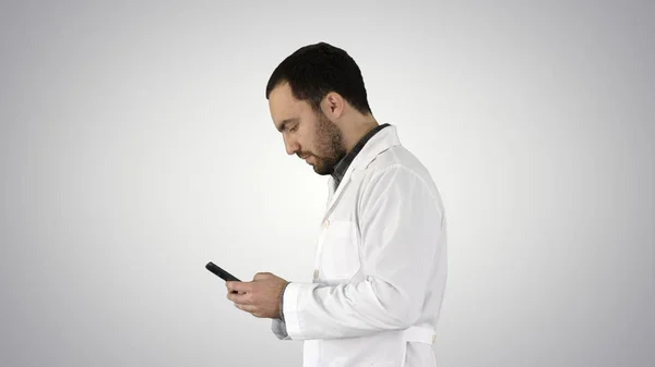 Camminare medico o infermiere sms su un telefono cellulare su sfondo gradiente . — Foto Stock