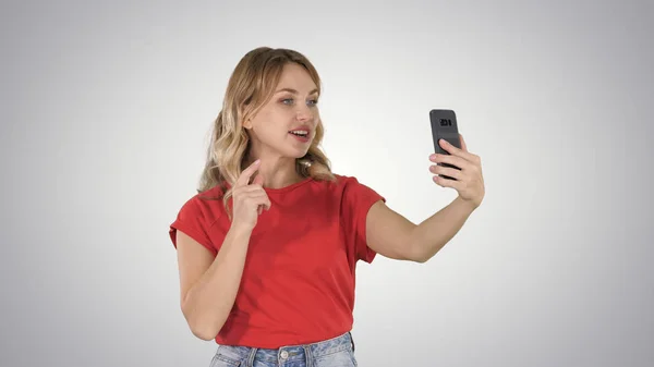 Cheerful female blogger recording video to front camera of modern telephone while walking on gradient background. — Stock Photo, Image