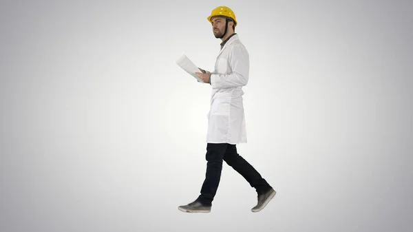 Engenheiro gerente andando com chapéu duro está segurando papel e verificando no fundo gradiente . — Fotografia de Stock
