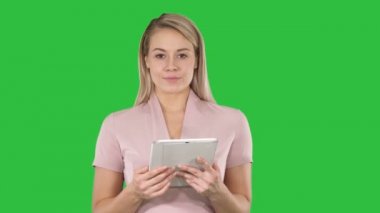 Güzel kadının sayfaları çevirme ve Chroma Key bir yeşil ekranda kamera seyir tablet kullanarak orta atış.