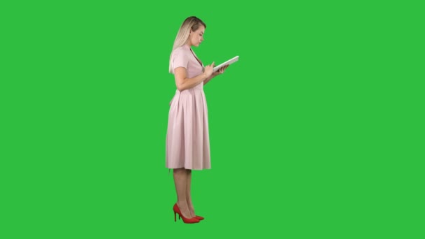 Mladá žena v růžových šatech bokorys pomocí tabletu na zelené obrazovce, Chroma Key. — Stock video