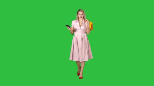 Shopping woman with bags texting message on smartphone while walking on a Green Screen, Chroma Key. — Stock Video