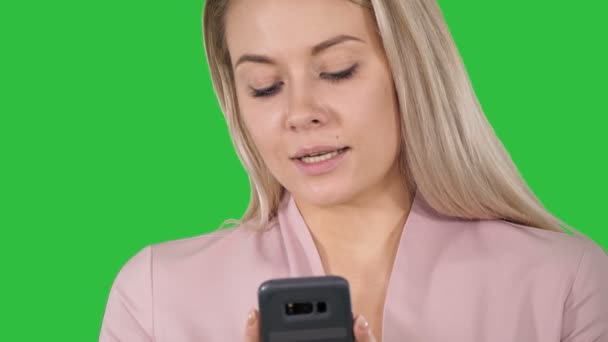 Trendy lachende blonde vrouw met haar mobiele telefoon glimlachen als ze een SMS-bericht op een groen scherm, Chromakey typen. — Stockvideo