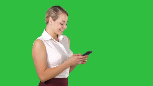 SMS an eine attraktive junge Frau, die ihr Smartphone in der Hand hält und es lächelnd betrachtet, während sie auf einem grünen Bildschirm steht, Chroma-Schlüssel. — Stockvideo