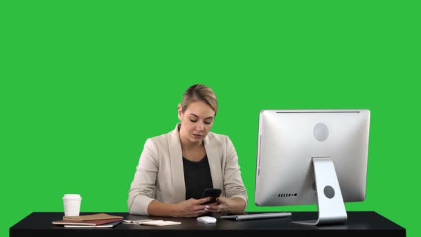 Beautiful businesswoman texting on her phone sitting at desk on a Green Screen, Chroma Key. — Stock Video