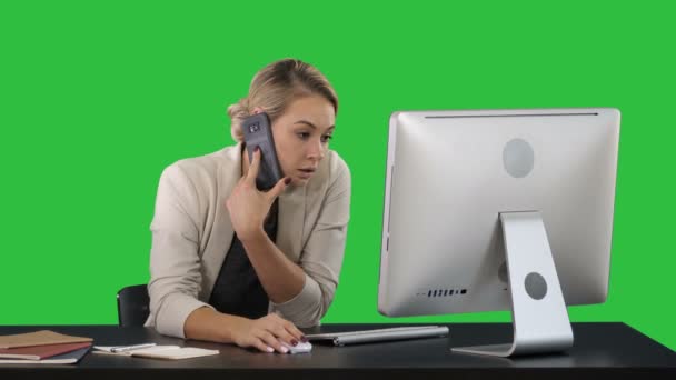 Jovem atraente conversando no telefone celular e sorrindo enquanto se senta em seu local de trabalho no escritório e olhando para o computador em uma tela verde, Chroma Key . — Vídeo de Stock