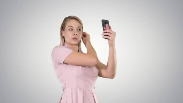 Mulher loira preening na frente do smartphone no fundo gradiente . — Vídeo de Stock