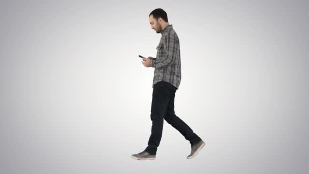 Joven hombre casual inteligente caminando y leyendo el mensaje en el teléfono celular en el fondo de gradiente . — Vídeos de Stock