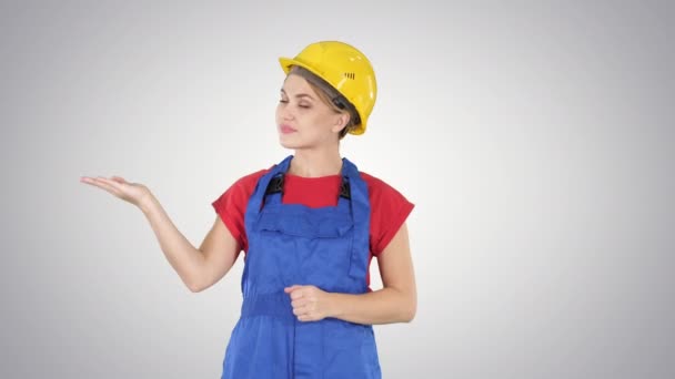 Bouwer van de jonge werknemer vrouw weergegeven: product presenteren met haar handen van haar kanten op de achtergrond met kleurovergang. — Stockvideo