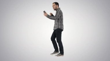 Yakışıklı sakallı adam gradyan arkaplanda yürürken akıllı telefonuyla video blogu kaydediyor.