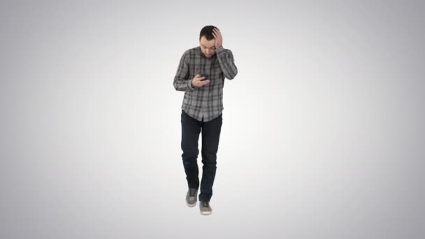 Sorprendido joven sosteniendo el teléfono y leyendo el mensaje al caminar sobre fondo degradado . — Vídeo de stock