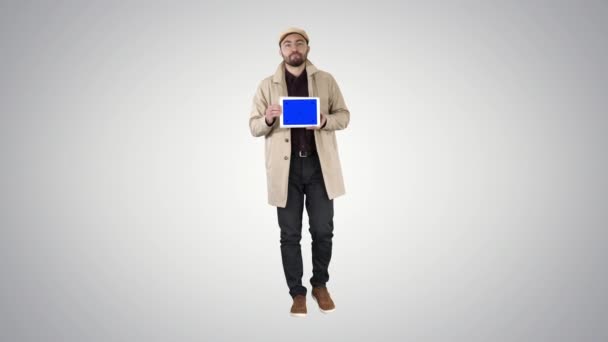 Молодой человек ходит, говорит и показывает цифровой планшет с синим экраном макета на градиентном фоне. — стоковое видео