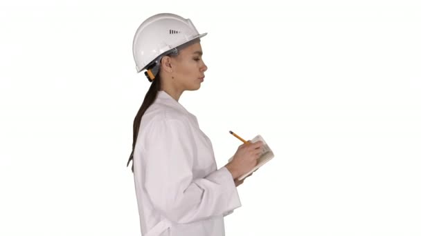 Femme ingénieur avec casque tient stylo et check-list mettre quelque chose vers le bas tout en marchant sur fond blanc. — Video