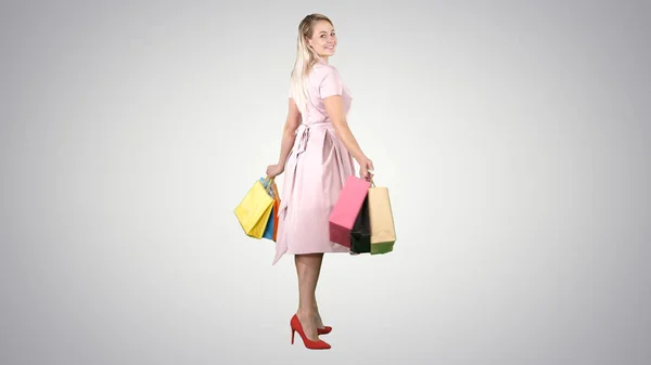 Happy young woman making a turn with shopping bags in her hands Looking at camera on gradient background. — Stock Photo, Image
