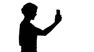 Yürüyüş ve fotoğraf çekmek ve selfies kadar bir akıllı telefon tutarak siluet güzel genç kadın.