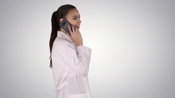 Mujer Dr sonríe mientras habla por teléfono, caminando sobre un fondo degradado . — Vídeos de Stock