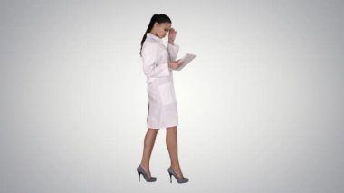 Tablet tableti kullanan ve gradyan arkaplan üzerinde yürüyen kadın doktor.