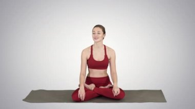 Yoga mat üzerinde oturan ve degrade arka plan üzerinde biriyle konuştuğunu güzel kadın.