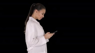 Neşeli genç bayan doktor yürürken telefonda yazı yazıyor, Alfa Kanalı.