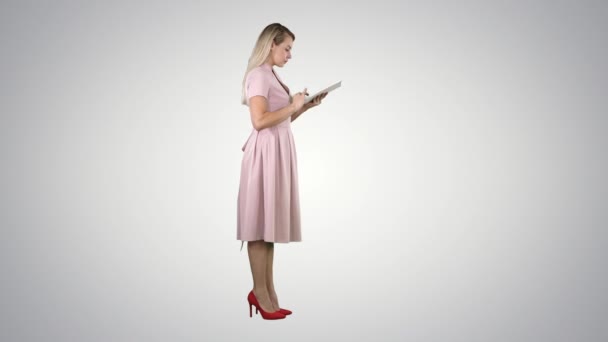 Ung kvinna i rosa klänning side se använda surfplatta på tonad bakgrund. — Stockvideo